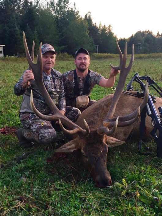 two men show off a bull elk they have harvested 